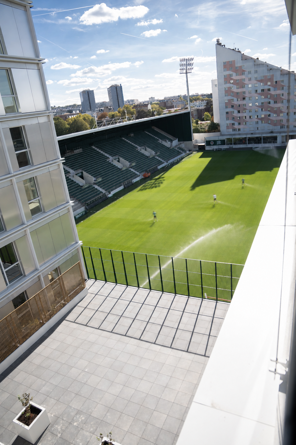 Vue en hauteur du terrain du stade Bauer, de ses tribunes et des immeubles environnants sous un ciel nuageux.
